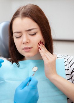 A woman rubbing her cheek during a dental emergency visit