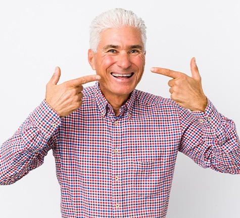 older man smiling and pointing to his face