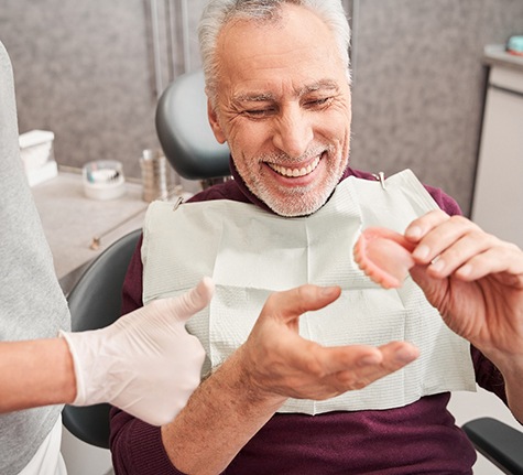mature patient holding dentures in the dentist chair