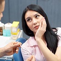 Woman in dental chair holding cheek