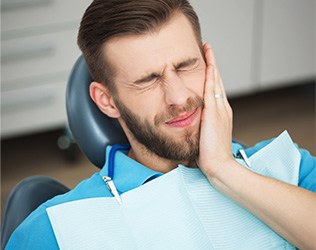 Man in dental chair holding cheek