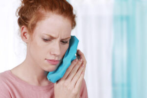 woman in dental pain holding a cold compress to her face